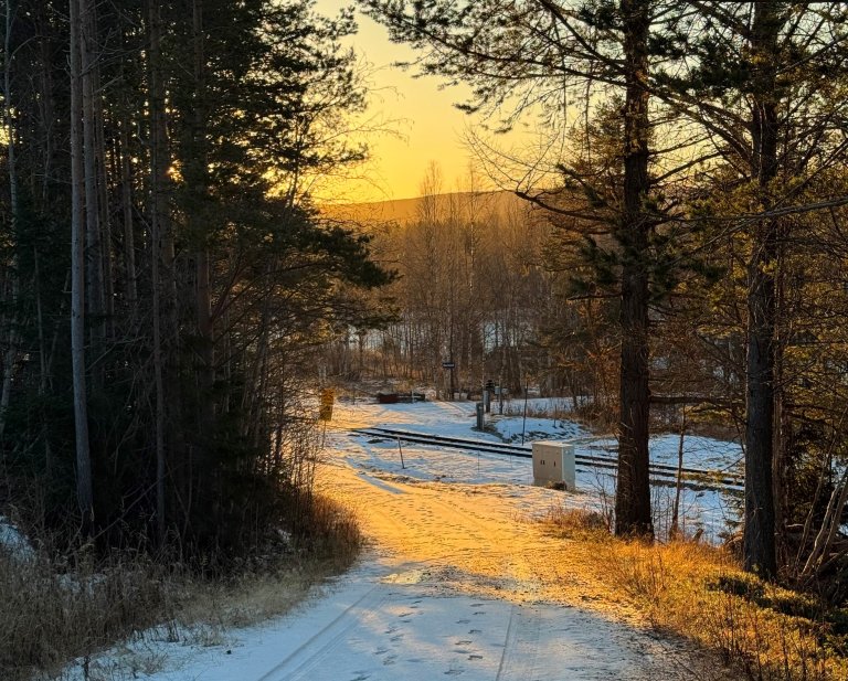 Foto av et vinterlandskap i Midt-Norge. Synlig på bildet er en vei, trær og jernbaneskinner, og fjell i det fjerne.